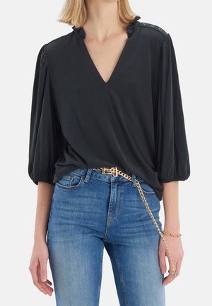 Blusa negra con escote en V y mangas abullonadas, con detalles de botones en los hombros. Combinada con jeans de mezclilla azul.