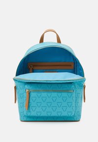 Turkos ryggsäck med ett strukturerat mönster, med bruna läderdetaljer, en baktill med dragkedja och ett rymligt inre fack.