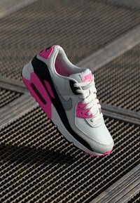 Nike sportbačiai su pilku tinkleliu, juodais akcentais, rožiniais akcentais ant pado ir prekės ženklo, su paminkštinta apykakle ir tekstūruota paviršiumi.