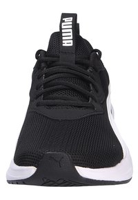 Chaussure de sport en mesh noir avec semelle blanche et accents noirs. Dispose d'un système de laçage et d'une languette avec un logo. Surface texturée.