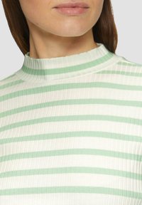 Haut à col montant côtelé présentant des rayures alternées vert clair et crème. Le matériau a une texture lisse avec une silhouette ajustée.