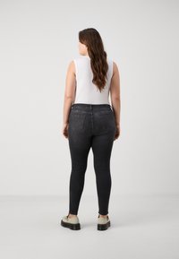 Fekete, skinny farmernadrág, hátsó zsebekkel és magas derék kialakítással. Fehér ujjatlan felsővel és bézs cipőkkel viselve.