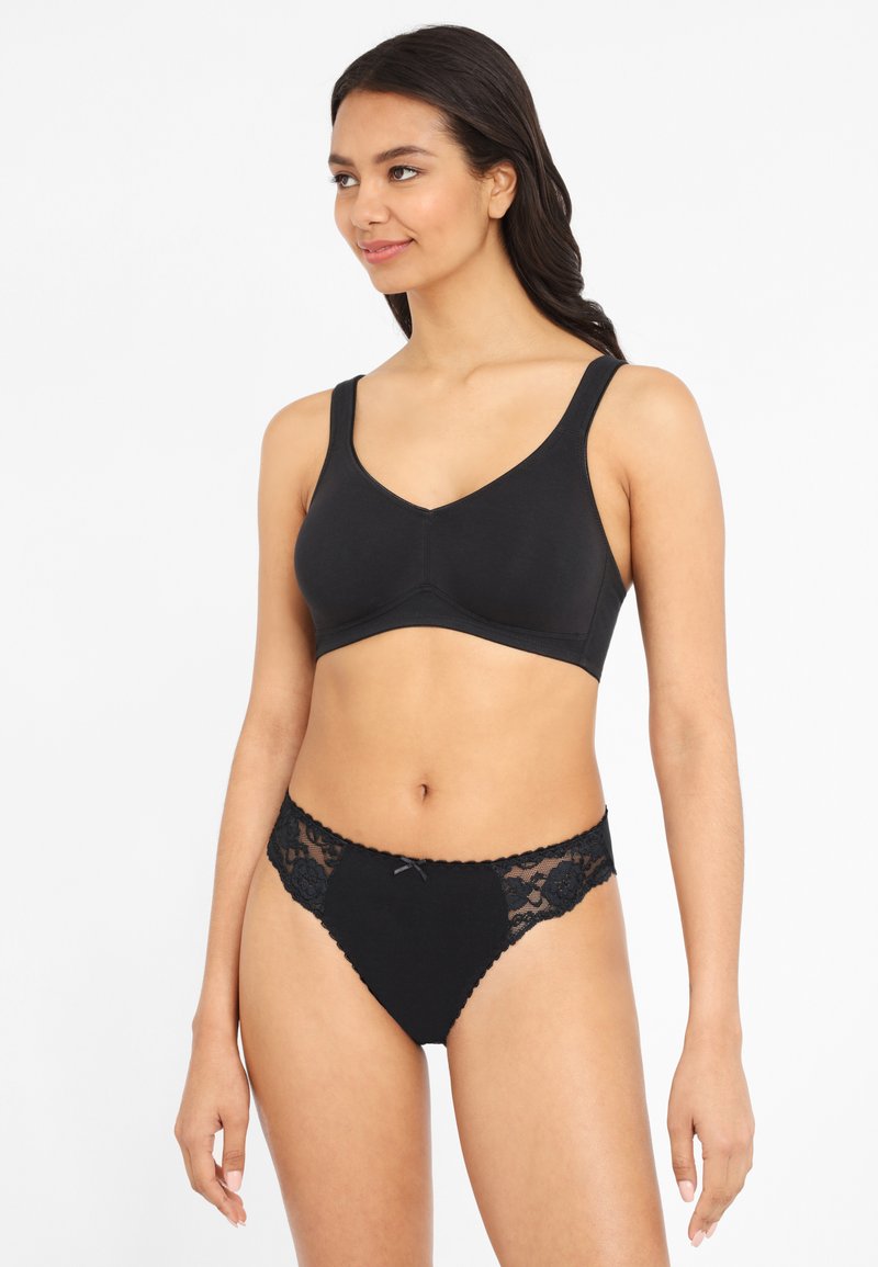 Svart trådlös bh med V-ringning och breda axelband, tillsammans med svarta trosor med spetsdetaljer som har blommönster och en mittslips.