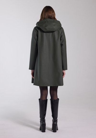 Groene waterdichte jas met een capuchon, voorzien van lange, rechte mouwen en een lengte tot halverwege de dij, gecombineerd met zwarte laarzen tot op de knie.