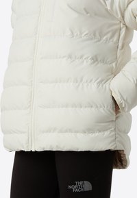 Εκρού μπουφάν τύπου puffer με σχεδιασμό καπιτονέ και κλείσιμο με φερμουάρ. Διαθέτει κρυφή τσέπη και απαλό υφή. Μαύρο λογότυπο στη κάτω γωνία.