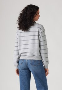 Sweatshirt gris avec des rayures horizontales bleu marine, avec des poignets et un ourlet côtelés, associé à un jean en denim bleu, vu de dos.