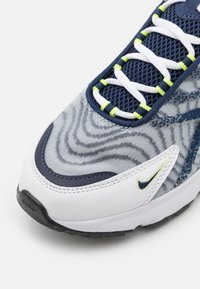 Sportschoen met een witte en marineblauwe bovenkant, textuur van blauw stof, mesh tong, groene accentveters en een zwarte rubberen outsole.