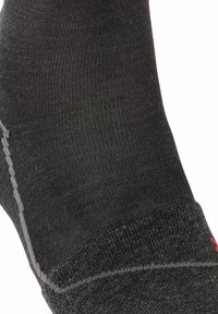 Calcetín negro hecho de un material suave y elástico; presenta una puntera reforzada, costuras grises y un pequeño logo rojo en el puño.
