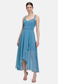Helles blaues, knielanges Kleid mit Rüschen-Trägern, figurbetontem Oberteil und asymmetrischem Saum. Aus weichem, fließendem Stoff gefertigt, mit einem schichtigen Design.