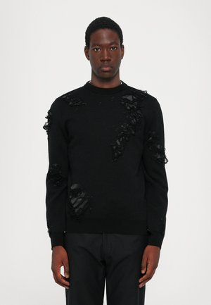 Schwarzer Pullover mit strukturiertem Design, Rüschendetails und Ausschnitten an der Vorderseite und den Ärmeln, aus einem weichen Material gefertigt.