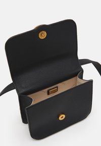 Černá texturovaná kožená taška přes rameno se zlatým patentkem, béžová vnitřní podšívka s potiskem "GUESS" a obdélníková nášivka s logem uvnitř.