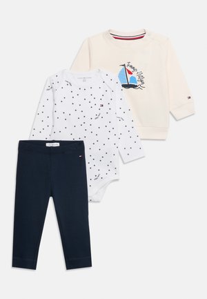 Ensemble bébé avec leggings côtelés bleu marine, body blanc à manches longues avec motif étoiles, et sweat crème avec motif voilier.