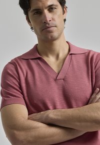 Polo de manga corta en rosa claro, con cuello en V y puños de canalé, fabricado en tejido de punto con un acabado texturizado.