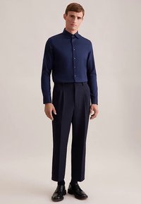 Camicia a maniche lunghe blu navy con collo a camicia e chiusura frontale con bottoni, abbinata a pantaloni blu navy sartoriali e scarpe di pelle nera. Tessuto dalla texture liscia.