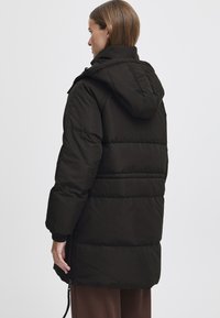 Čierna puffrová bunda s kapucňou, s prešívaným dizajnom, elastickými manžetami a bočnými vreckami na zips, zobrazená z zadného uhla.
