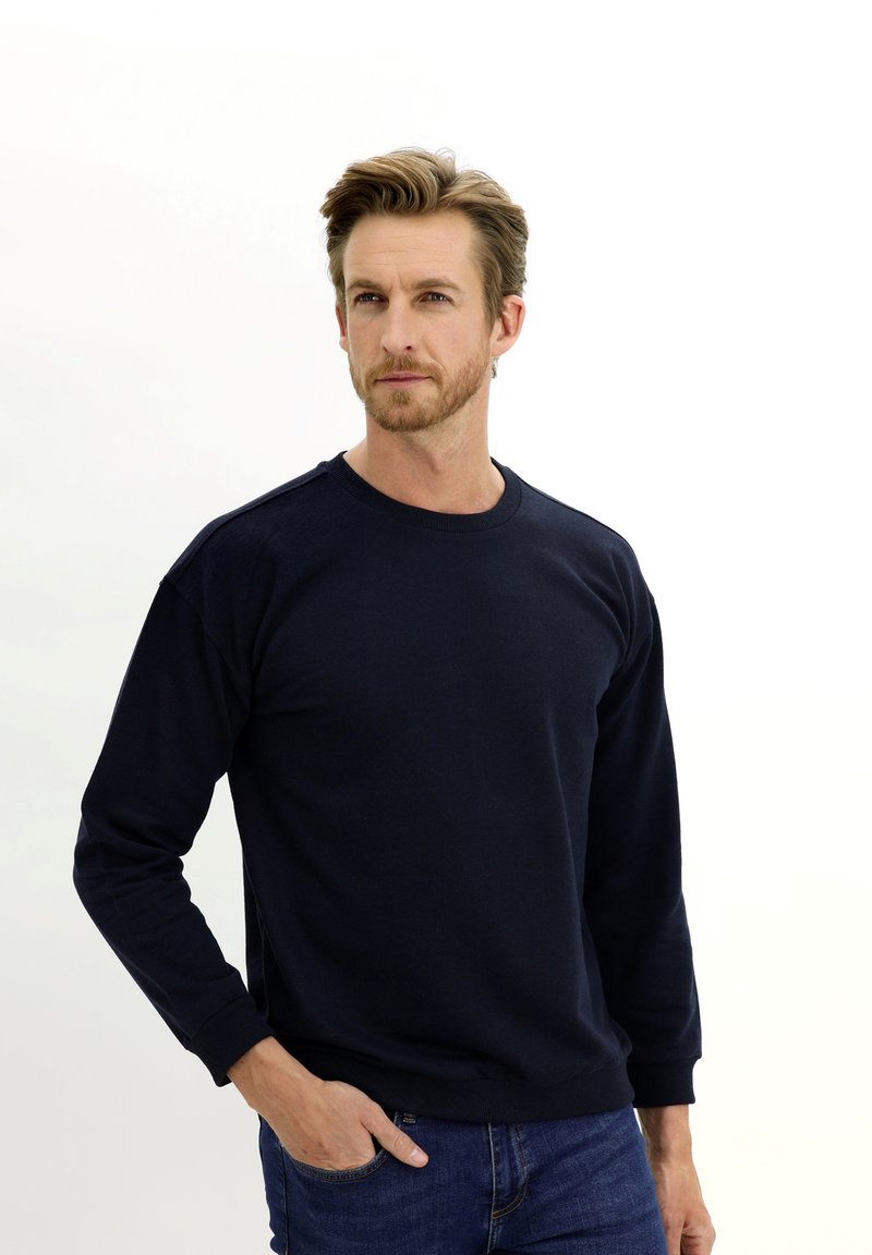 Sudadera de manga larga azul marino de mezcla de algodón, con cuello redondo y puños acanalados. Se lleva con jeans de denim azules.
