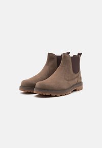 Bocanci din suede maro, cu panouri elastice pe lateral, vârf rotund și o talpă din cauciuc texturată. Include o bandă de prindere pentru o îmbrăcare ușoară.