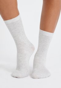 Calcetines gris claro con un acabado suave y texturizado y puño blanco acanalado, mostrando ligera variación de color a lo largo de la tela.