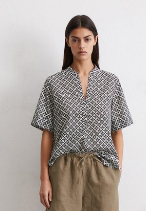 Short-sleeved blouse in a black and white geometric pattern, with a V-neckline, made of lightweight fabric, paired with beige linen pants.