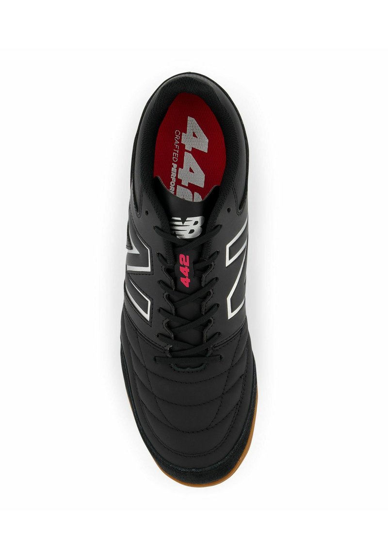 Chaussure de football noire avec texture matelassée, logo blanc et accents rouges à l'intérieur. Elle présente des lacets noirs et une semelle extérieure en caoutchouc gomme.