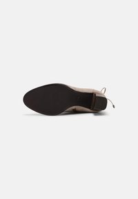 Bottine en daim beige avec un bout pointu et un talon discret. La semelle en caoutchouc noir présente un design texturé pour une meilleure adhérence.