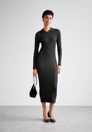 Dark green ribbed knit dress with long sleeves and scalloped edges, paired with a black handbag and black heels.