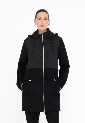 Cappotto nero con cappuccio caratterizzato da una parte superiore trapuntata a rombi, dettagli dorati, due tasche frontali e una zip a tutta lunghezza.