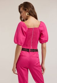 Top rosa con maniche a sbuffo e scollatura quadrata, caratterizzato da una schiena arricciata e chiusura con zip, abbinato a pantaloni sartoriali a vita alta.