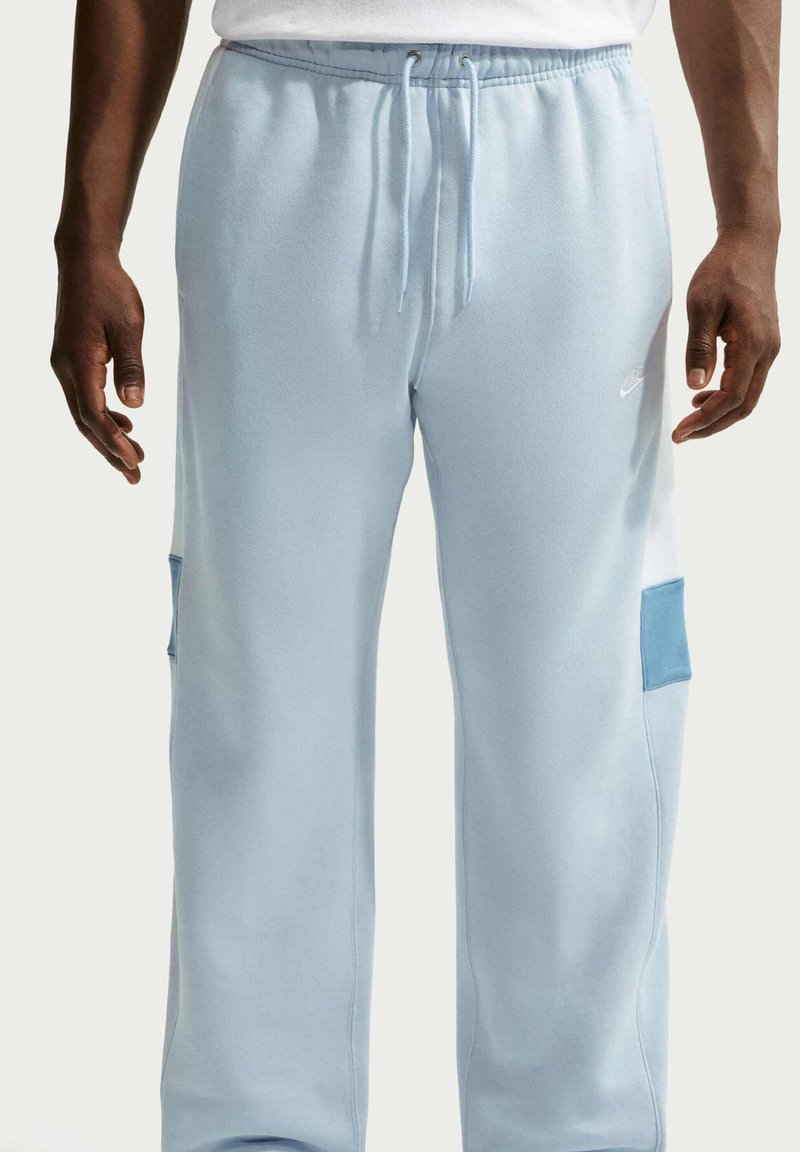 Persoon draagt lichtblauwe joggingbroek met trekkoord, lichtblauwe opgestikte zakken op de benen en een wit shirt, getoond van taille tot voeten.