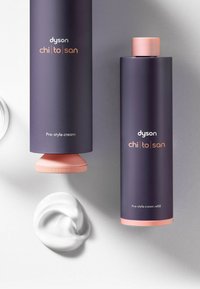 Ricarica crema pre-styling Dyson Chi|to|san, contenitore cilindrico viola con tappo rosa, accompagnato da una spirale di crema bianca su una superficie argentata.