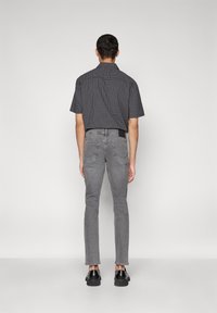 Kortermet rutete skjorte i svart og blå, kombinert med slim-fit grå denimjeans og svarte sko. Synlige detaljer på baksiden av jeansene.