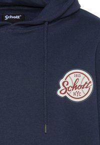 Granatowa bluza z kapturem wykonana z bawełny, wyposażona w przednią kieszeń, regulowany kaptur ze sznurkiem oraz okrągłą naszywkę z logo z czerwonymi i białymi akcentami.