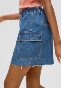 Jupe en denim avec un ourlet effiloché, une taille élastique et une grande poche plaquée. Le tissu est bleu moyen avec des coutures orange contrastantes.