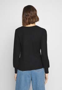 Top nero a maniche lunghe con costine, scollatura rotonda e spalle a sbuffo. Indossato con jeans in denim a vita alta azzurri.