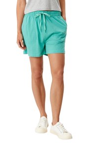 Turkusowe szorty wykonane z miękkiego materiału, z elastycznym paskiem w talii, sznurkiem do regulacji i dwoma bocznymi kieszeniami. Połączone z białymi trampkami.