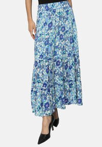 Jupe maxi florale avec un design en étages. Présente des motifs floraux bleus et blancs. Fabriquée en tissu léger, associée à des talons noirs.