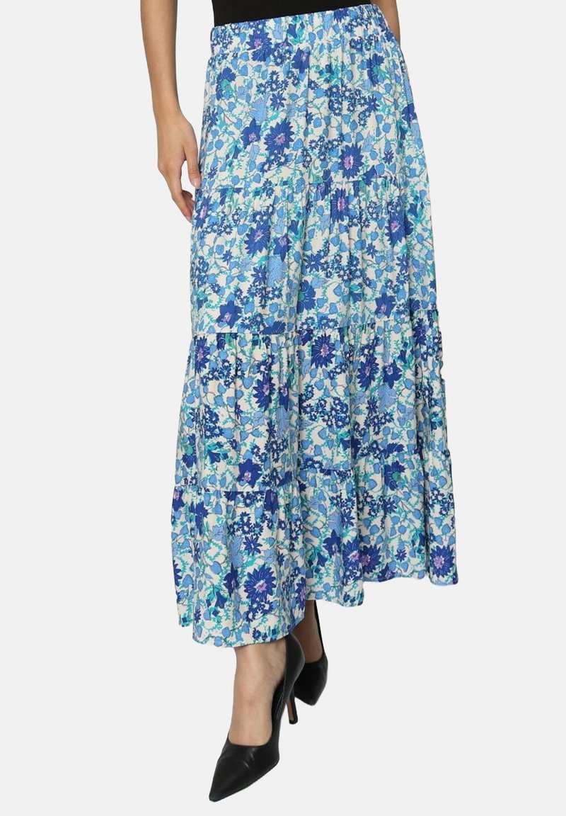 Jupe maxi florale avec un design en étages. Présente des motifs floraux bleus et blancs. Fabriquée en tissu léger, associée à des talons noirs.