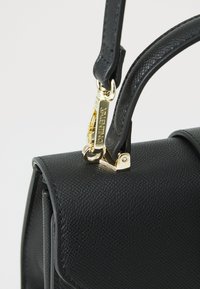 Bolso de mano de cuero negro texturizado con un gancho de cierre y herrajes en tono dorado, que presenta una forma estructurada y un único asa superior.