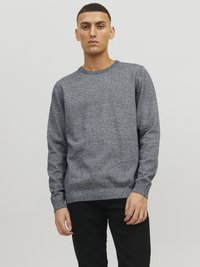 Grijze gebreide crewneck trui met een textuurpatroon; lange mouwen; geribbelde manchetten en zoom; gedragen over zwarte broek.