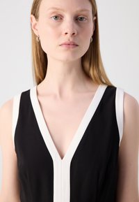 Robe noire sans manches avec un décolleté en V profond, accent blanc le long des bords, texture lisse, design minimaliste et silhouette ajustée.