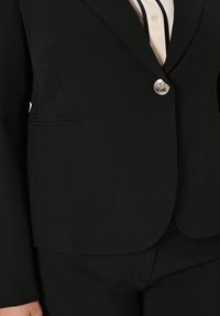 Schwarzer Blazer mit taillierter Passform, einem glänzenden Knopfverschluss und dezenten Seitentaschen. Glattes Material mit matter Oberfläche und scharfen Revers.