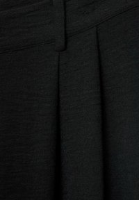 Detail blízkého záběru černé tkaniny s texturovaným povrchem a sklady, což dodává strukturovaný design. Materiál vypadá lehce a jemně.