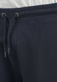 Jogging en bleu marine avec un tissu texturé, une taille élastique à cordon de serrage avec des accents métalliques, et de subtils détails de couture sur le côté.