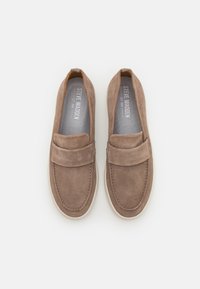 Des chaussures slip-on en daim brun avec un col rembourré, des coutures décoratives et une semelle en caoutchouc de couleur claire. L'intérieur présente un imprimé de logo.