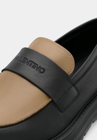 Černo-hnědá kožená mokasína se širokým černým páskem s rytým nápisem „Valentino“, hladkou texturou a kulatou špičkou.