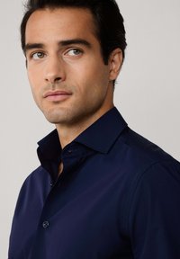 Camisa de vestir azul marino con cuello abotonado, textura suave y un diseño ajustado, con un detalle de un solo botón cerca del cuello.