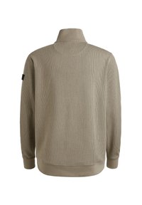 Sudadera beige de canalé con cuello alto, mangas largas y un parche de logo negro en la manga izquierda. Textura suave y corte relajado.