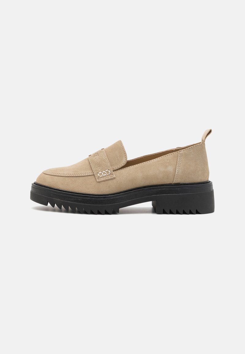 Beige suede loafers with a wide strap and decorative stitching, featuring a thick black rubber sole with a serrated edge.