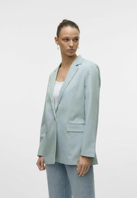 Blazer azzurro chiaro in tessuto liscio, chiusura a un bottone, due tasche frontali e rever a punta, abbinato a una maglietta bianca e jeans.