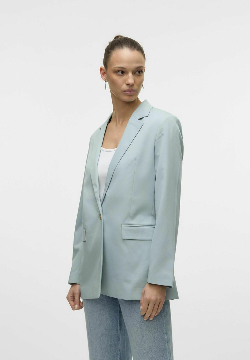 Blazer azzurro chiaro in tessuto liscio, chiusura a un bottone, due tasche frontali e rever a punta, abbinato a una maglietta bianca e jeans.